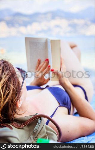 Young beautiful woman in bikini reading a book on the beach