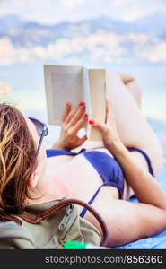 Young beautiful woman in bikini reading a book on the beach