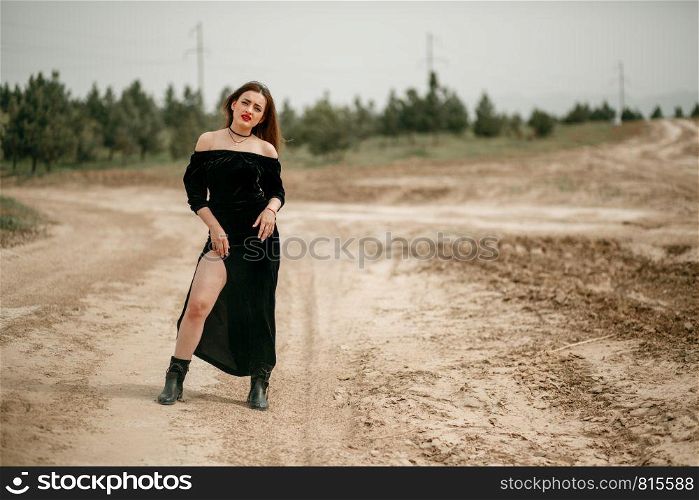Young beautiful woman in black dress posing for a photographer on a sandy road.