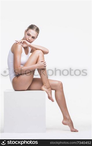 Young beautiful woman in cotton underwear sitting on white cube. Woman in cotton underwear