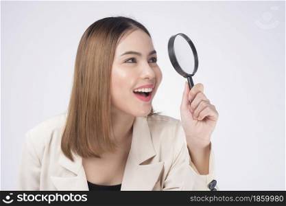 Young beautiful woman in suit holding magnifying glass over white background studio