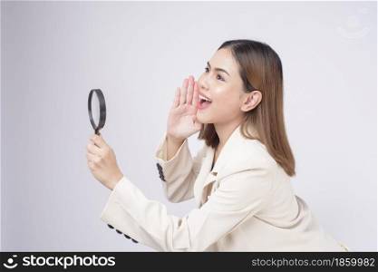 Young beautiful woman in suit holding magnifying glass over white background studio