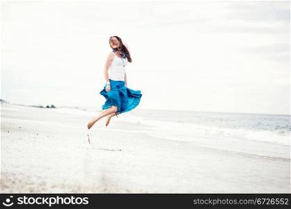 Young beautiful woman in white cami and turquoise skirt has fun on the ocean shore