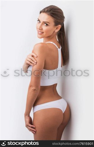 Young beautiful woman in white cotton underwear touching own skin standing , white background. Woman in underwear touching skin
