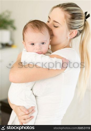 Young beautiful woman kissing her baby boy on hands