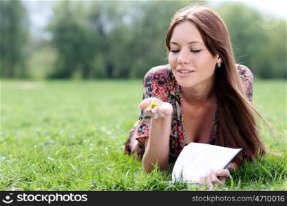Young beautiful woman lays on a grass in park with a diary in hands &#xA;