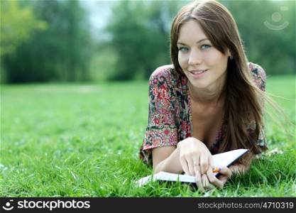 Young beautiful woman lays on a grass in park with a diary in hands &#xA;
