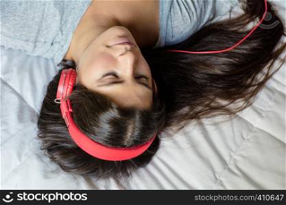 Young beautiful woman lying on bed and listening to music with headphones. Smiling woman enjoying music.