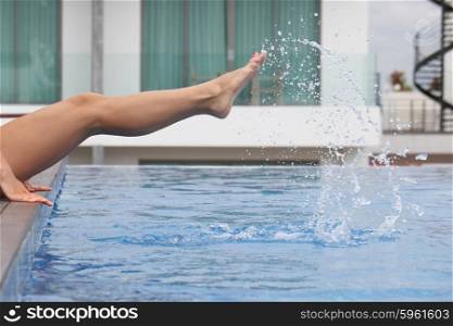 Young beautiful woman making water splash with legs at the pool. Woman making water splash in pool