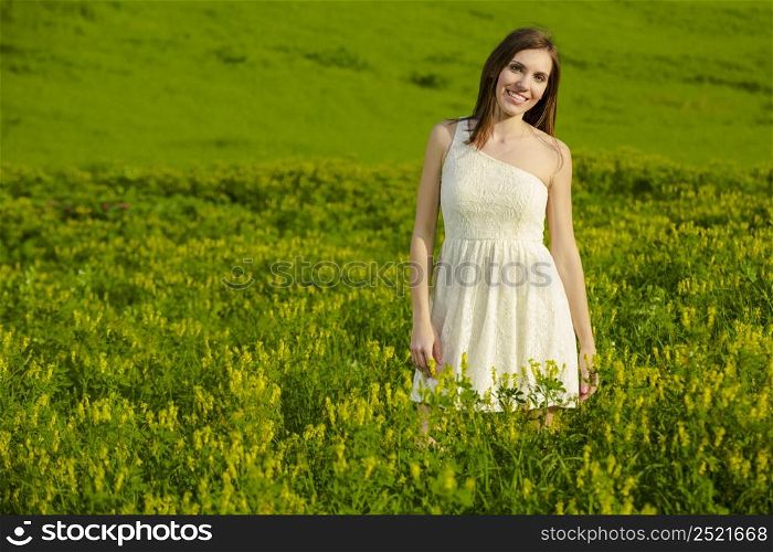 Young beautiful woman on a green meadow wearing a white dress