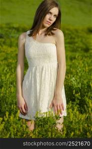 Young beautiful woman on a green meadow wearing a white dress