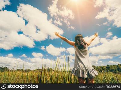 Young beautiful woman on green grass meadow spreading arms to the blue sunny sky on summer day. Getaway and meditation concept.