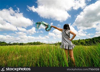 Young beautiful woman on green grass meadow spreading arms to the blue sunny sky on summer day. Getaway and meditation concept.