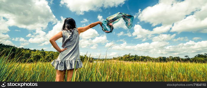 Young beautiful woman on green grass meadow spreading arms to the blue sunny sky on summer day. Getaway and meditation concept.