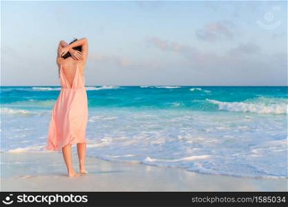Young beautiful woman on the beach. Back view of happy girl oat sunset. Woman laying on the beach enjoying summer holidays looking at the sea