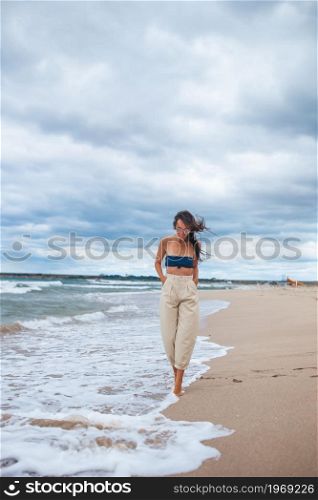 Young beautiful woman on the beach in windy and cloudy weather. Young woman on the beach in the storm