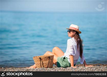 Young beautiful woman on the beach sunbathers. Concept of health beach vacation - sun creams, straw hat, sunglasses . Young woman in hat on the beach vacation