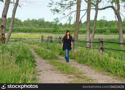 Young beautiful woman on the walk on the road in the middle of dandelion meadow.