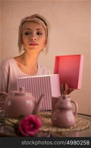 Young beautiful woman opening gift box while having tea-party. She is very satisfacted. Valentine's day or international women's day celebration.