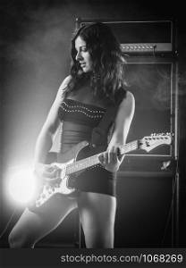 Young beautiful woman playing an electric guitar in front of large amplifier done in black and white.