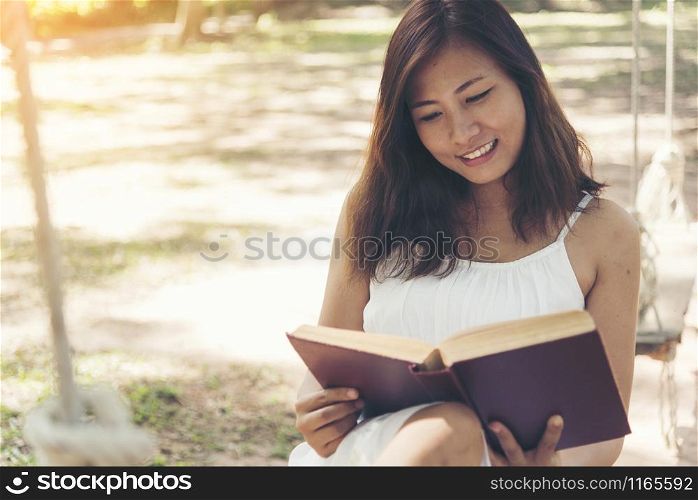 Young beautiful woman reading a book in the park with smiling face.