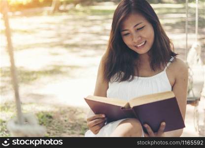 Young beautiful woman reading a book in the park with smiling face.