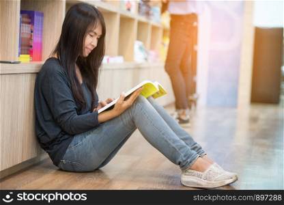 Young beautiful woman reading book while sitting on floor in library