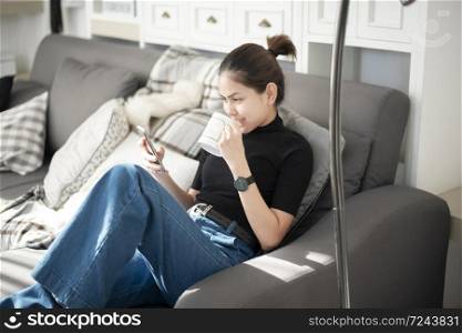 Young beautiful woman relaxing on sofa at home and using smart phone