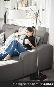 Young beautiful woman relaxing on sofa at home and using smart phone