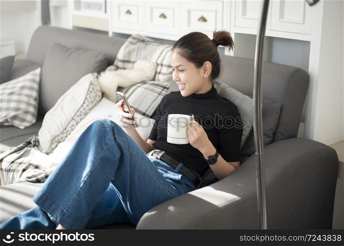 Young beautiful woman relaxing on sofa at home and using smart phone