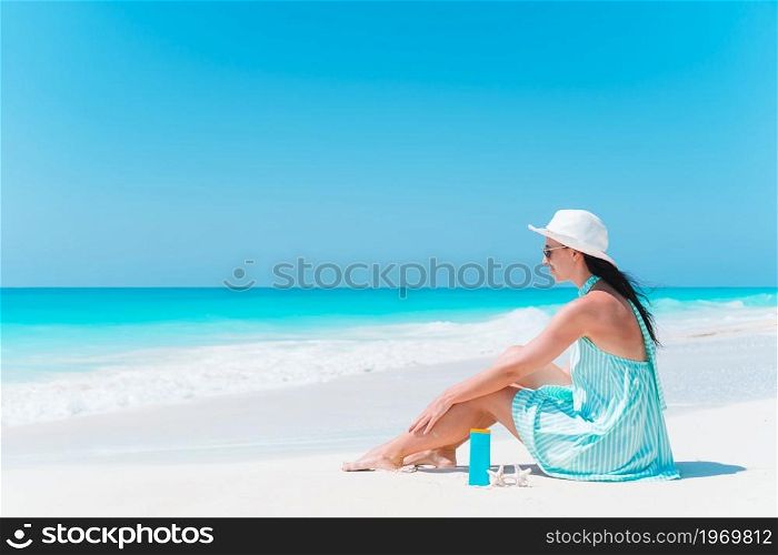 Young beautiful woman relaxing on the beach. Suncream near the woman. Woman laying on the beach enjoying summer holidays looking at the sea