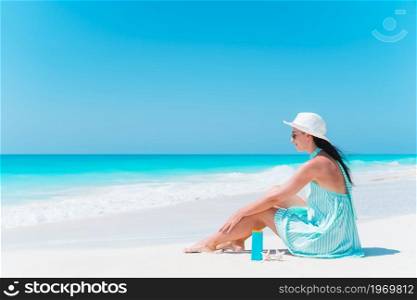 Young beautiful woman relaxing on the beach. Suncream near the woman. Woman laying on the beach enjoying summer holidays looking at the sea