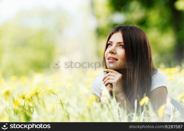 Young beautiful woman resting on fresh green grass with flowers