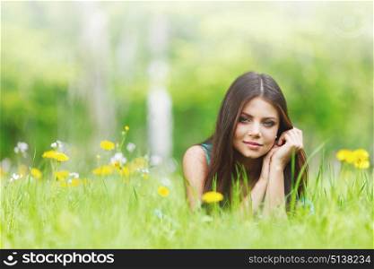 Young beautiful woman resting on fresh green grass with flowers. Woman on flower field