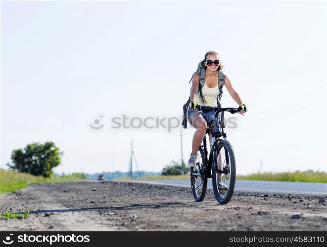 Young beautiful woman riding a bicycle on road. Summer bike walk