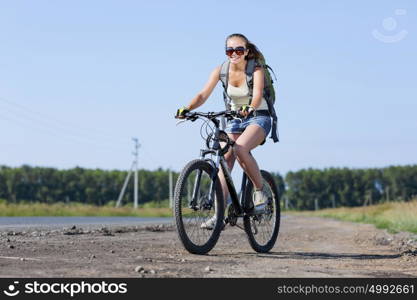 Young beautiful woman riding a bicycle on road. Summer bike walk