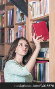 Young beautiful woman selecting a red book from a library. A concept for education or leisure activities.