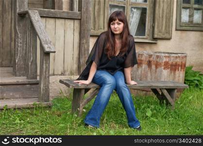 Young beautiful woman sit on the bench in front of old house.