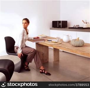 Young beautiful woman sitting in kitchen and reads the magazine