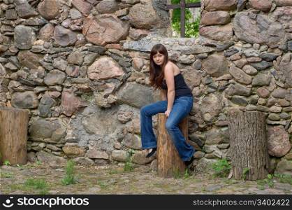 Young beautiful woman sitting on the log near old castle ruins.