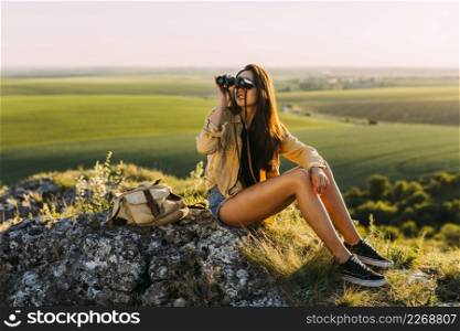 young beautiful woman sitting rock looking through binocular