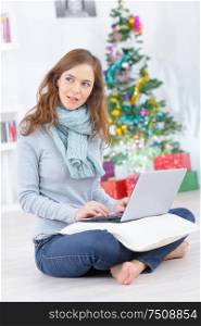 young beautiful woman sitting with laptop near christmas tree