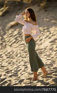 Young beautiful woman standing on the sand of the beach wearing casual clothes.. Young beautiful woman standing on the sand of the beach