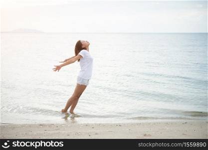 Young beautiful woman standing stretch her arms in the air on the beach with barefoot. Relaxing holiday.