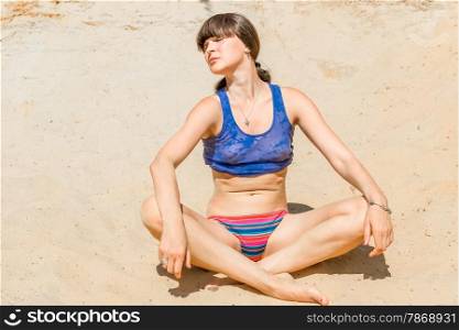 young beautiful woman sunbathing on the sand in the lotus position