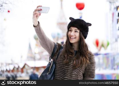 Young beautiful woman tourist taking pictures on mobile phone on the background Red Square, Moscow Kremlin, Russia