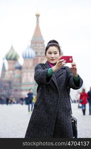 Young beautiful woman tourist taking pictures on mobile phone on the background Red Square, Moscow Kremlin, Russia