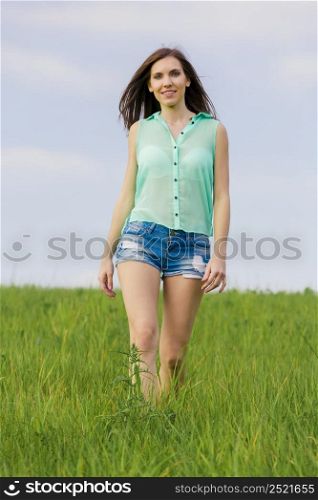 Young beautiful woman walking on a green meadow