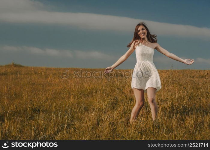 Young beautiful woman walking on a meadow wearing a white dress