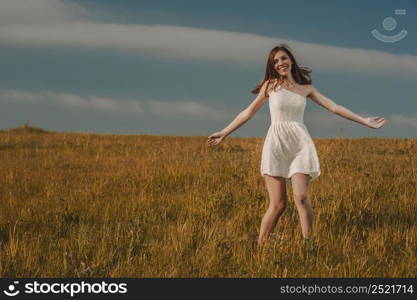 Young beautiful woman walking on a meadow wearing a white dress